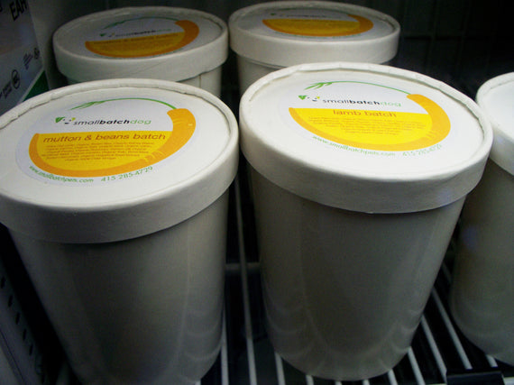 White smallbatch containers of dog food on a fridge shelf.