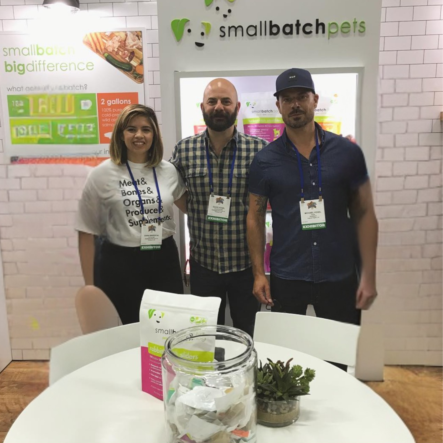 Three people standing in a smallbatch booth with promotional materials on a table.