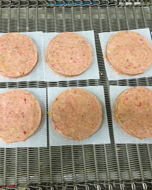 Six raw dog food patties on a conveyor belt.