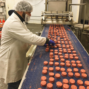 Person in a food processing plant inspecting round red products on a conveyor belt.